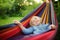 Cute little blond caucasian boy enjoy and having fun with multicolored hammock in backyard or outdoor playground. Summer active