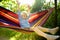 Cute little blond caucasian boy having fun with multicolored hammock in backyard or outdoor playground. Summer active leisure for