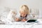 Cute little blond child, toddler boy, reading book with white puppy maltese dog