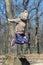 Cute little blond kid girl having fun outdoors. Child in casual sport wear and kerchief jumping high from tree stump in forest