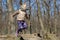 Cute little blond kid girl having fun outdoors. Child in casual sport wear and kerchief jumping high from tree stump in forest