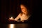 The cute little blonde girl is looking on the light of candle over dark background