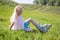 Cute little blonde girl sitting on green grass and putting on roller skates - leisure, childhood, outdoor games and sport concept