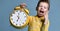 Cute little boy with alarm clock,isolated on blue. Funny kid pointing at alarm clock at 7 o`clock at morning.
