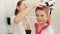 Cute little boy in bathrobe looking in reflection in mirror while mother drying his hair with hairdryer in bathroom