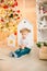 Cute little boy with blond hair plays with  toys in a bright room decorated with Christmas garlands near the Christmas tree.