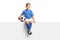 Cute little boy in a blue soccer jersey sitting on a blank panel and smiling at camera