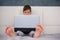 Cute little boy child Laying on the bed at home looking at laptop computer screen. Selective focus on bare foot