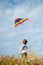 Cute little boy with colorful kite in one hand flying in air in summer sunset blue sky
