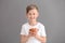 Cute little boy with cup of hot cocoa drink on grey background