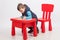 Cute little boy drawing, red table and chair, on white background. Childhood education concept