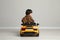 Cute little boy driving children`s electric toy car near grey wall indoors, back view