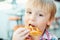 Cute little boy eats tasty belgian waffle on summer terrace.