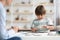 Cute little boy exercising with professional kids tutor at preschool, playing with wooden figures at desk, empty space