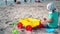 Cute little boy with headscarf playing with colorful toys on beach sand
