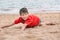 Cute little boy lies on the sand on the seashore happy,