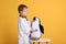 Cute little boy in pediatrician`s uniform playing with stethoscope and toy penguin on yellow