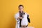 Cute little boy in pediatrician`s uniform playing with stethoscope and toy penguin on yellow