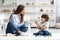 Cute little boy playing with colorful blocks, young professional woman kids psychologist writing notes in notepad