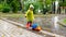 Cute little boy in raincoat and rubber boots blaying with toy truck in big puddle at park