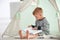 Cute little boy reading book in hovel at home