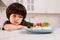 Cute little boy refusing to eat dinner in kitchen