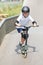 A cute little boy rides a scooter in a skatepark