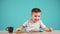 Cute little boy sitting at table and playing on tablet. Child is drinking tea.