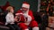 Cute little boy tells Santa Claus about his dreams and receives cherished gift. Grandson and grandfather in a red suit