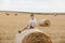 A cute little boy in a white t-shirt and khaki shorts is sitining on round bales of hay. Photo session in the field