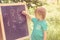 Cute little boy writing letters and numbers at blackboard in the garden. Toned.