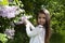 Cute little brunette girl, dressed in a white shirt , she holds a blossoming branch of lilac