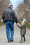 Cute little caucasial boy with blue eyes looks back walking with old-aged man, holding him with hand. Stroll in autumn park, casua