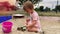 Cute Little caucasian baby girl in pink dress plays in sandbox with shovel and bucket outdoors