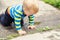 Cute little caucasian blond toddler boy having fun lying in a puddle after rain outdoors. Curious child discovering