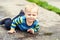 Cute little caucasian blond toddler boy having fun lying in a puddle after rain outdoors. Curious child discovering world in mud