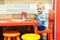 Cute little caucasian blond toddler boy sitting at table and drawing at children area at retail clothes store. Baby spending time