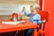 Cute little caucasian blond toddler boy sitting at table and drawing at children area at retail clothes store. Baby spending time