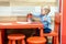 Cute little caucasian blond toddler boy sitting at table and drawing at children area at retail clothes store. Baby spending time