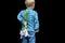 Cute little child boy holding bouquet of wild flowers behind his back on black background. Surprise, gift for your loved one,