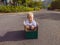 Cute little child boy sitting inside cardboard box on silent street in modern comfortable cottage village. Childhood and