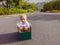 Cute little child boy sitting inside cardboard box on silent street in modern comfortable cottage village. Childhood and