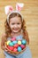 A cute little child girl with bunny ears sits on the floor with a basket of Easter eggs