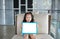 Cute little child girl holding empty white blackboard on fabric sofa in library room