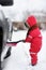 Cute little child helping to brush a snow from a car