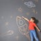 Cute little child playing with chalk rocket drawing on grey