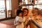 Cute little curly girl 3 years old with a young red-haired mother in the bakery at the counter chooses pastries. Cafe