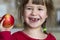 A cute little curly toothless girl smiles and holds a red apple. Portrait of a happy baby eating a red apple. The child loses milk