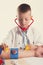 Cute little doctor boy with smile on face sitting at his desk on white background. Intelligent children in doctor suit with blue