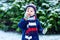 Cute little funny child in colorful winter fashion clothes having fun and playing with snow, outdoors during snowfall